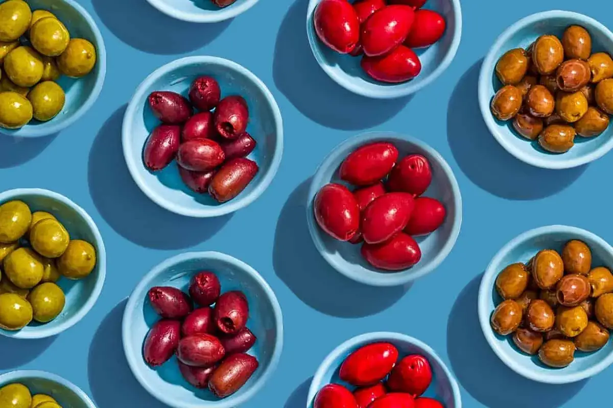 Różne rodzaje oliwek w miseczkach. Czy oliwki są lekkostrawne? Zielone, czerwone i brązowe oliwki na niebieskim tle.