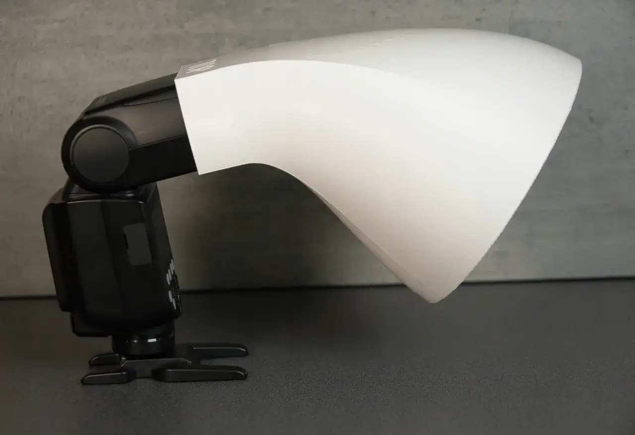 Biały, zakrzywiony dyfuzor do makro zamontowany na czarnej lampie błyskowej.