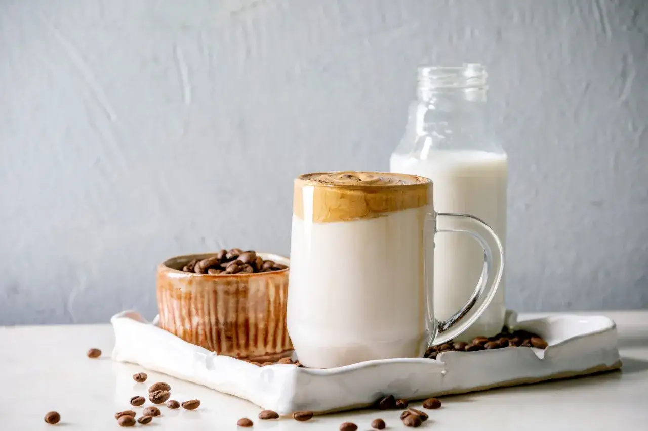 Kawa z mlekiem roślinnym, ziarna kawy i butelka mleka. Czy kawa z mlekiem roślinnym jest zdrowa?