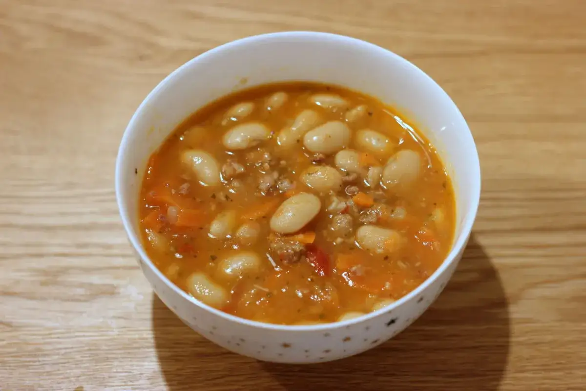Miseczka sycącej zupy serbskiej z białej fasoli, mięsa mielonego i warzyw na drewnianym tle.