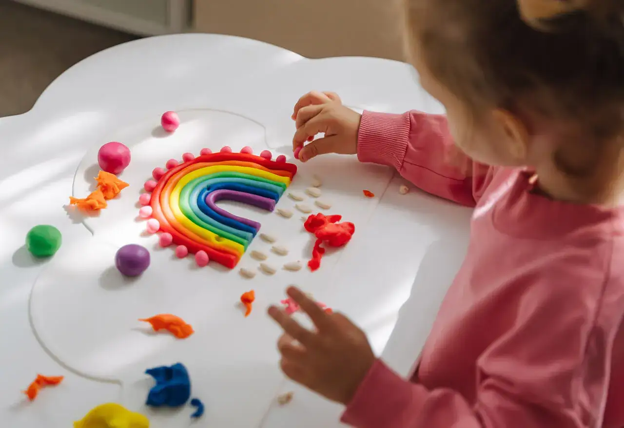 Dziecko tworzy tęczę z plasteliny. To świetny sposób, jak prowadzić zajęcia z dziećmi, rozwijając ich kreatywność i zdolności manualne.