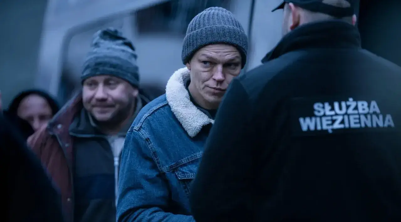 Mężczyzna w czapce i dżinsowej kurtce patrzy na funkcjonariusza Służby Więziennej. Scena z jednego z polskich seriali Canal Plus.