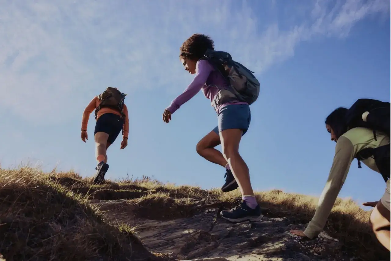 Trzy osoby wspinają się po wzgórzu. Jedna z nich ma na sobie bluzkę z wełny z merynosa, która zapewnia komfort podczas wędrówki.