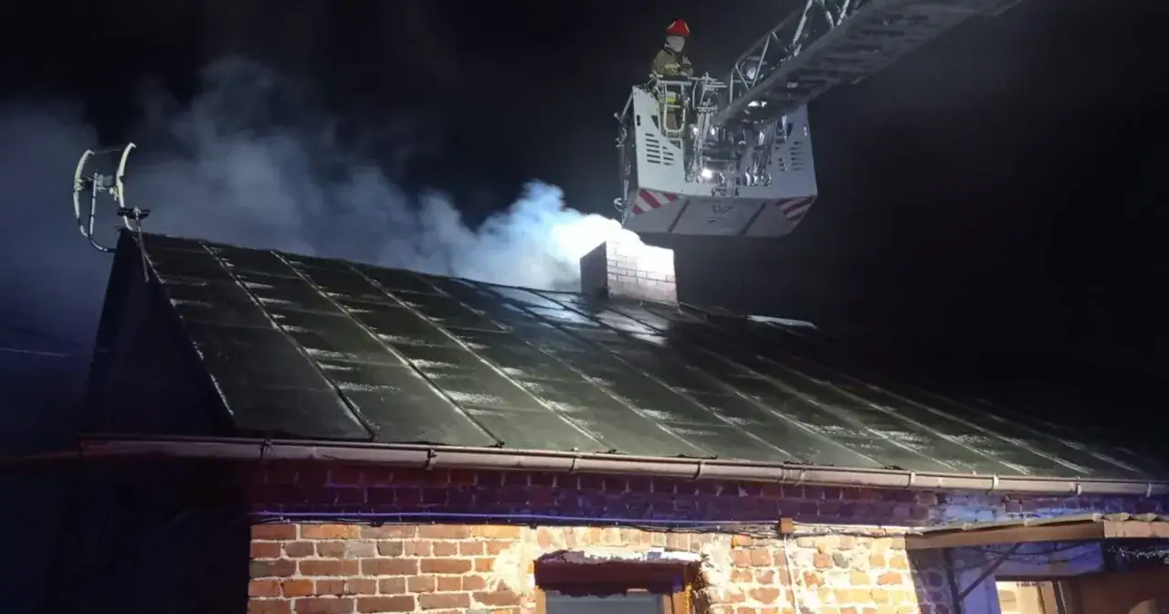 Strażak na podnośniku sprawdza, czy komin powinien być ciepły, gdy z dachu unosi się dym.