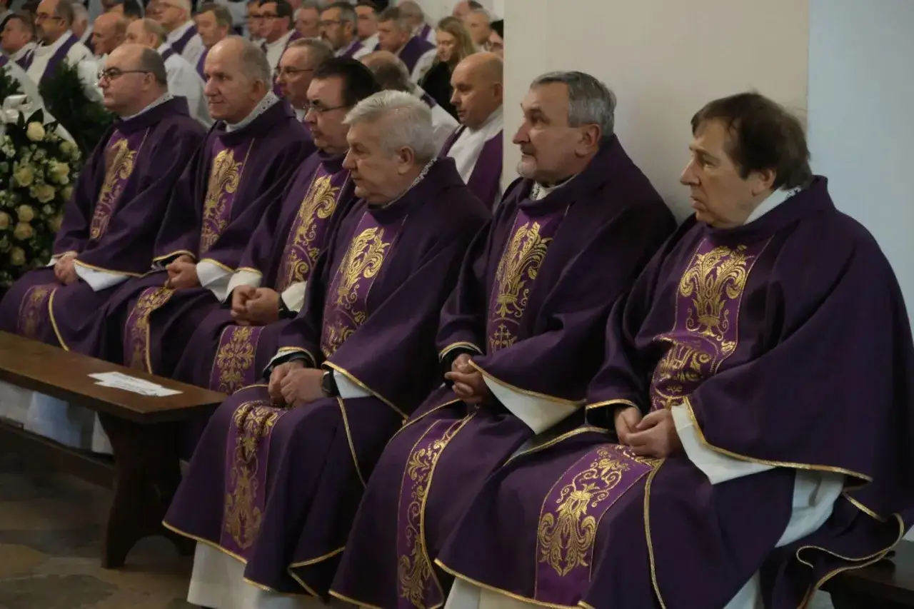Księża w fioletowych szatach siedzą w ławce. Zastanawiają się, ile trwa różaniec na pogrzebie, modląc się za zmarłego.