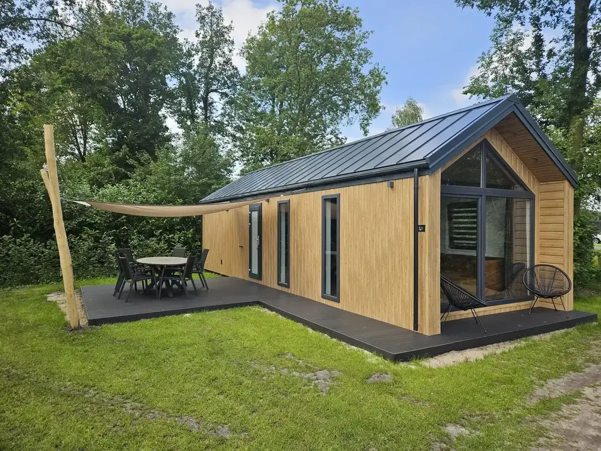 Nowoczesny domek letniskowy na zgłoszenie, z tarasem i meblami ogrodowymi, otoczony zielenią.