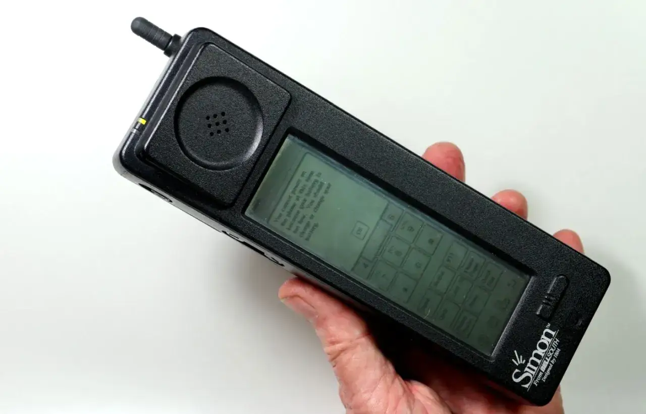 Dłoń trzyma IBM Simon, pierwszy telefon dotykowy z 1992 roku, z ekranem pokazującym komunikat o baterii.