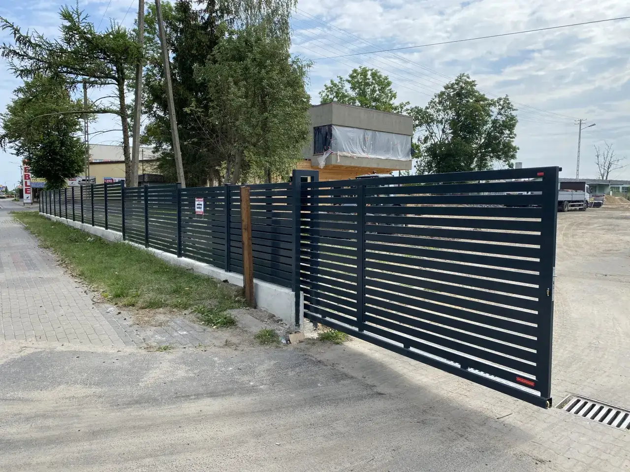 Nowoczesne ogrodzenie z bramą, idealne do zabezpieczenia działki. Zastanawiasz się, ile kosztuje ogrodzenie działki? Sprawdź!