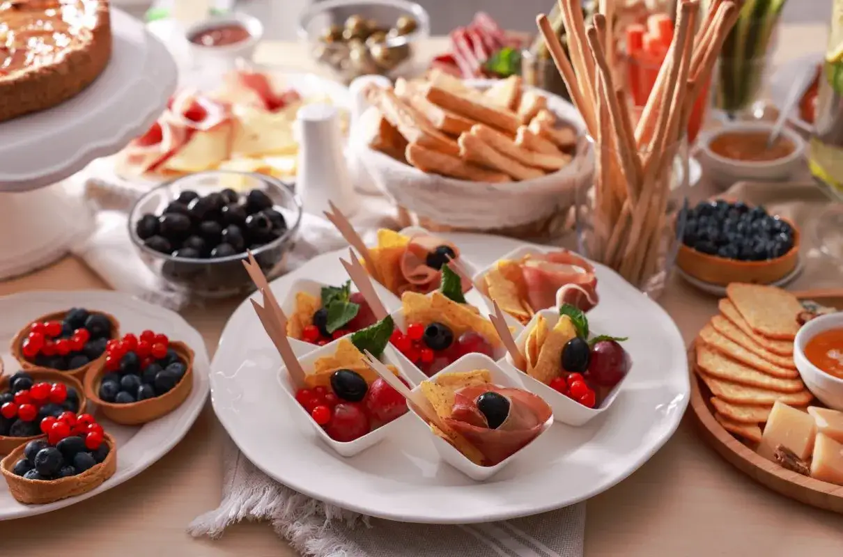 Eleganckie przekąski na ciepło do wódki: mini tartaletki z owocami, koreczki z wędliną i owocami, paluszki grissini, oliwki i ser.