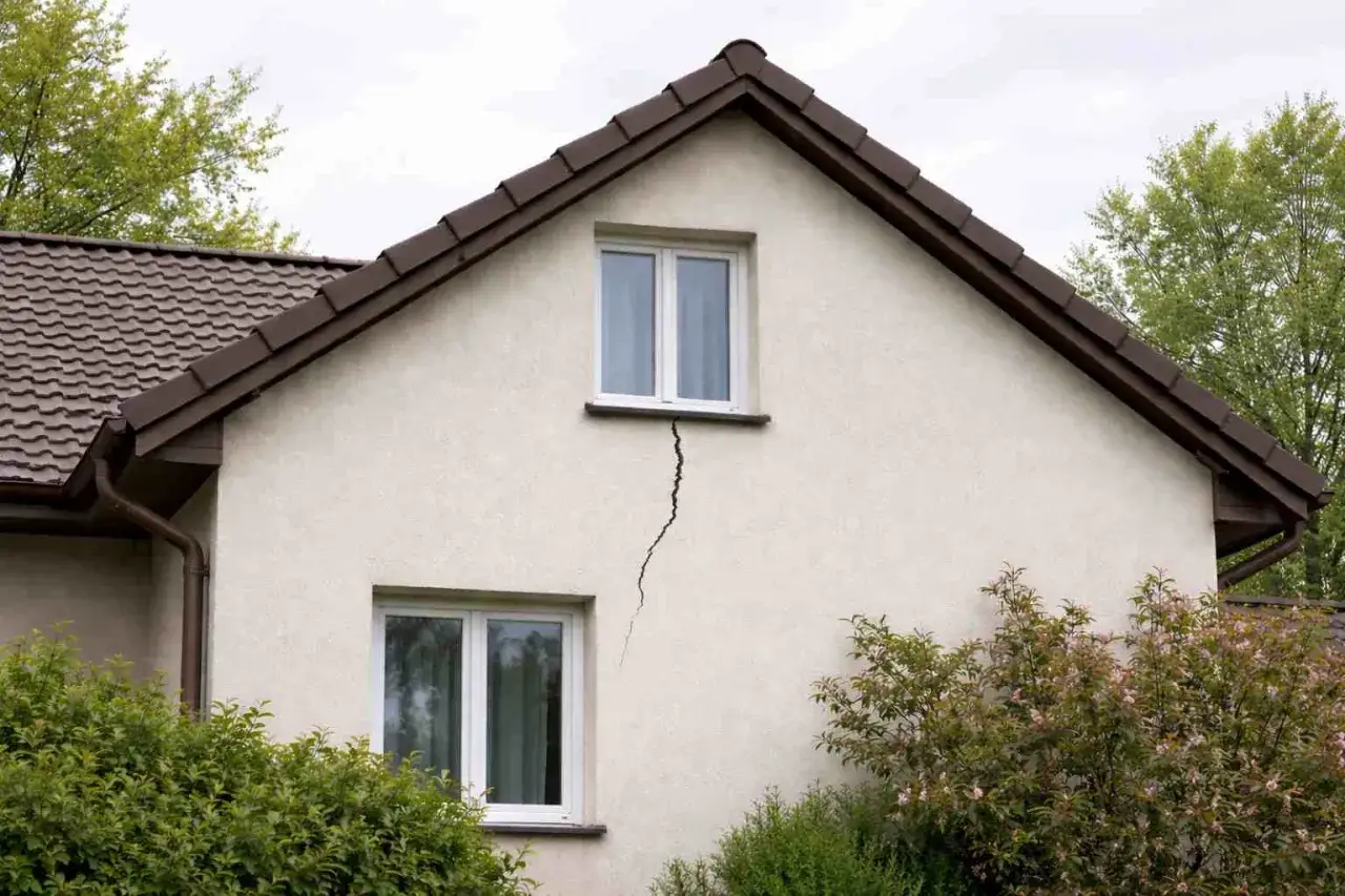 Widoczna ściana szczytowa budynku z dwoma oknami. Pomiędzy oknami biegnie wyraźne pęknięcie elewacji.