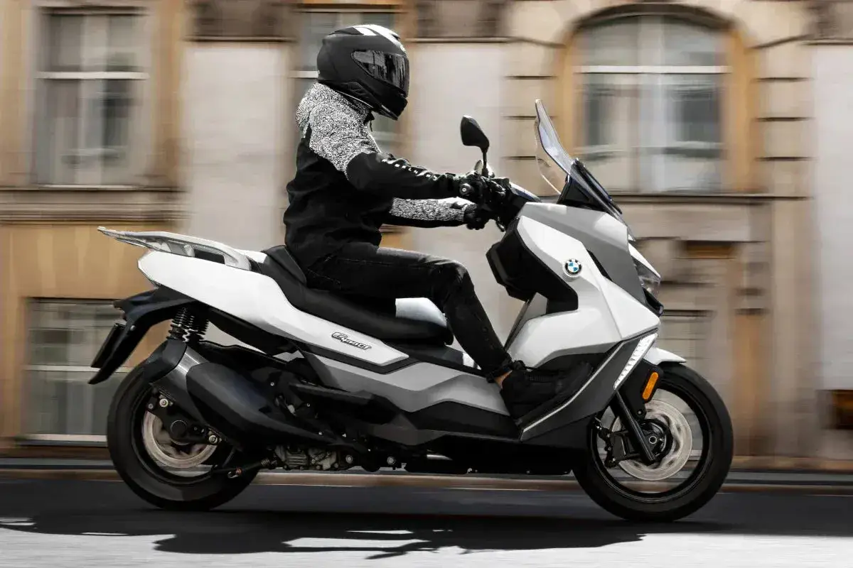 Osoba w kasku jedzie nowoczesnym, białym motorowerem BMW po mieście.