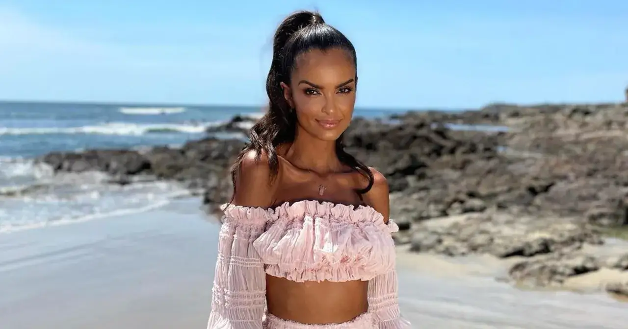 Uśmiechnięta kobieta w r&oacute;żowym, falbaniastym topie na plaży. Idealne miejsce na wakacje w hotelu Paradise 7.