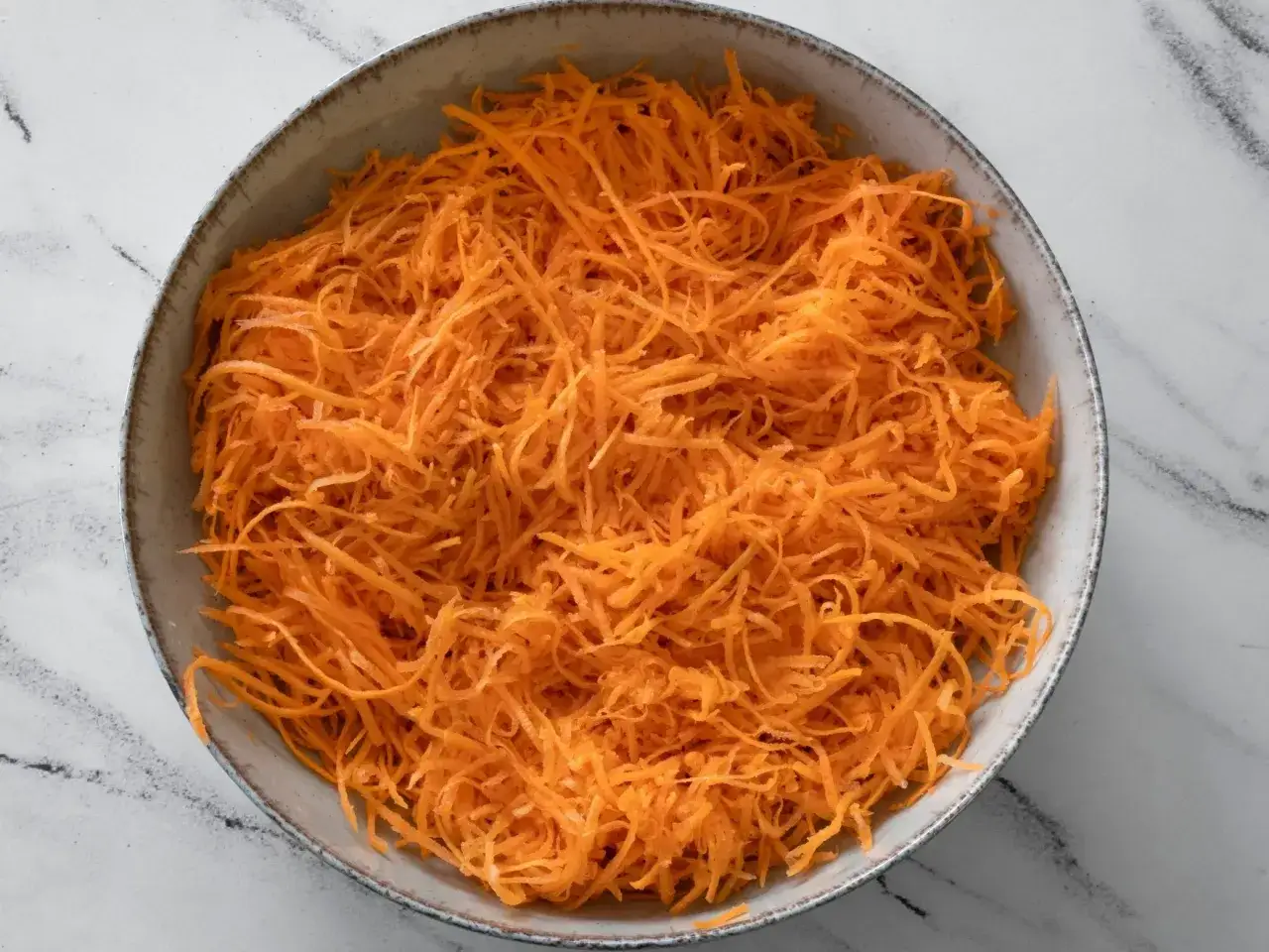 Miseczka pełna startej marchewki, gotowa na surówkę z marchewki jak z restauracji.
