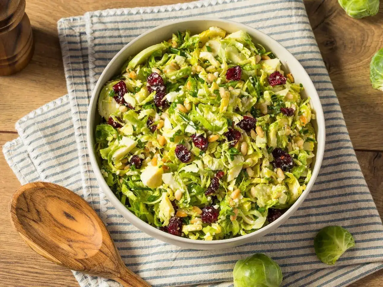 Pyszna sałatka z brukselką, żurawiną i orzeszkami pinii, podana w misce na drewnianym stole.