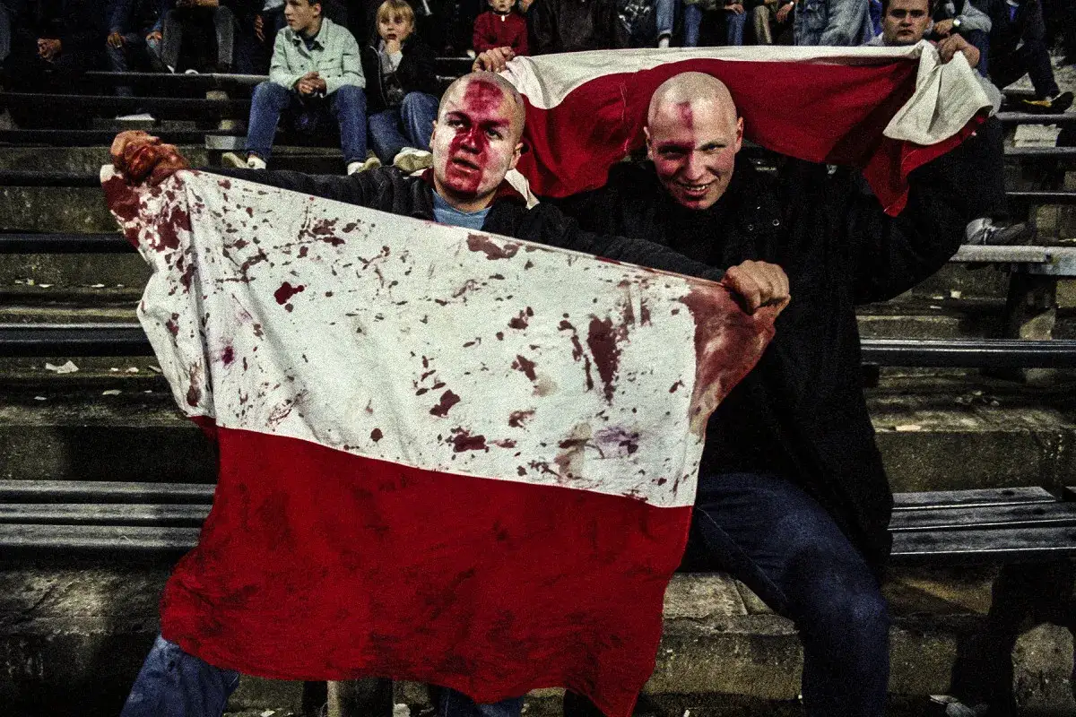 Dw&oacute;ch mężczyzn z zakrwawionymi twarzami trzyma polską flagę. Mariusz Forecki uchwycił ten moment.