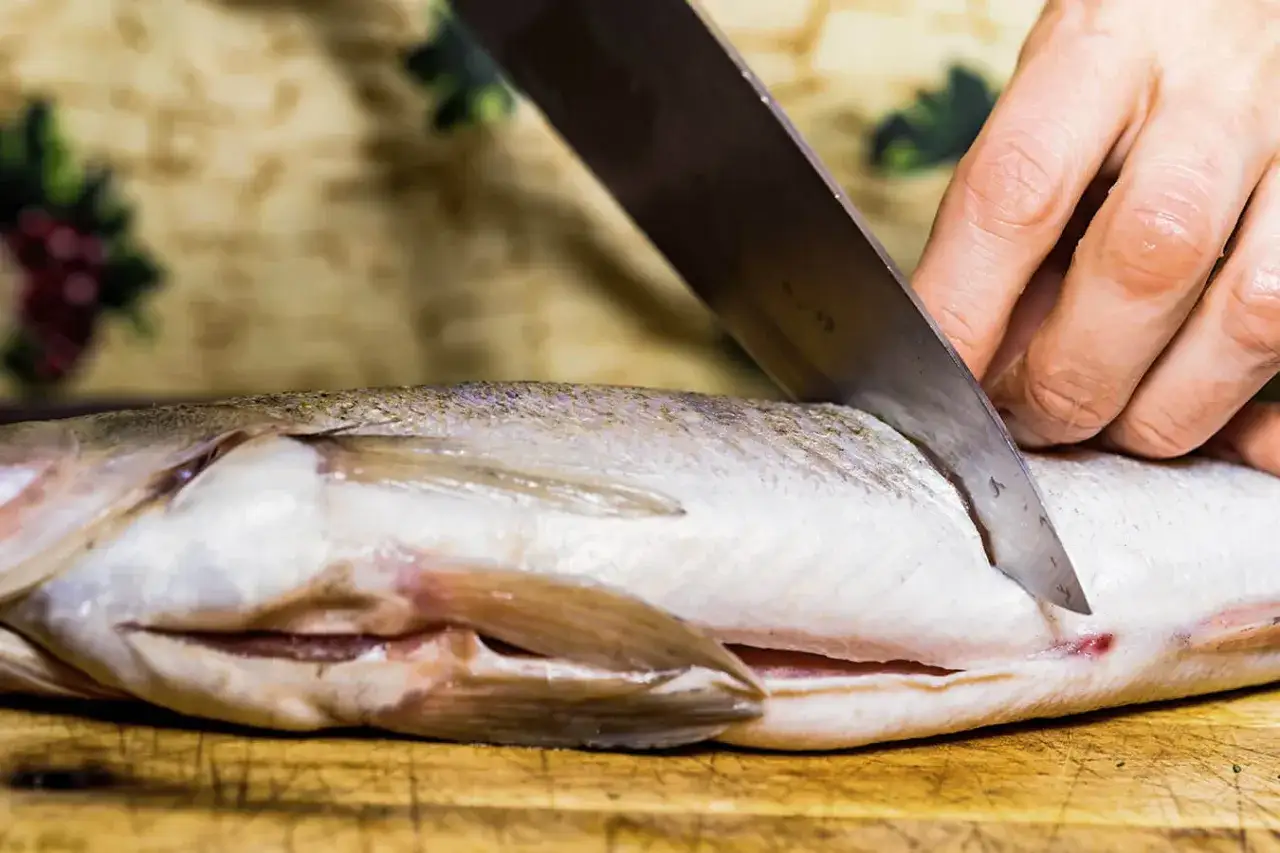 Przygotowanie karpia do zamrożenia: ostry nóż kroi rybę na desce.