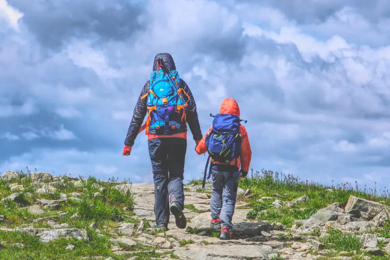 Dwie osoby, dorosły i dziecko, idą kamienistym szlakiem w g&oacute;rach. To idealny widok dla tych, kt&oacute;rzy zastanawiają się, jak zacząć chodzić po g&oacute;rach.