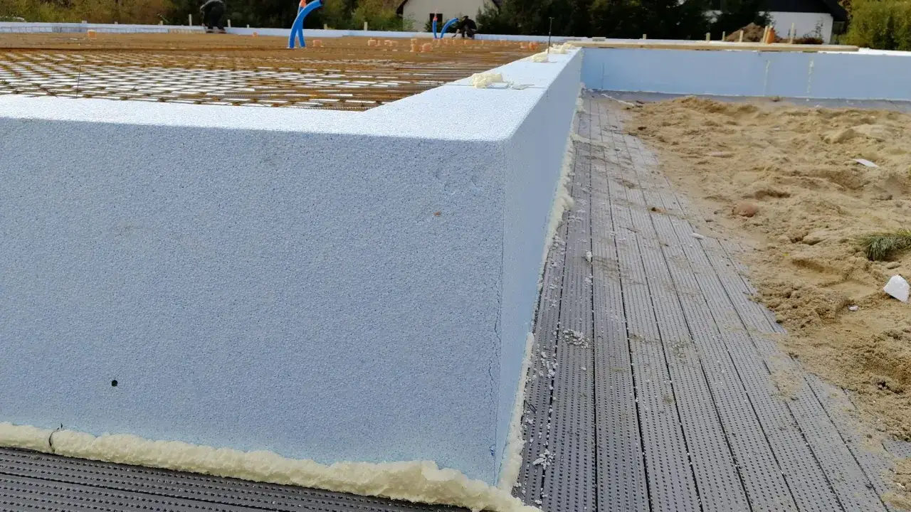 Budowa fundamentów: niebieski styrodur na fundamenty tworzy izolację, obok zbrojenie i piasek.