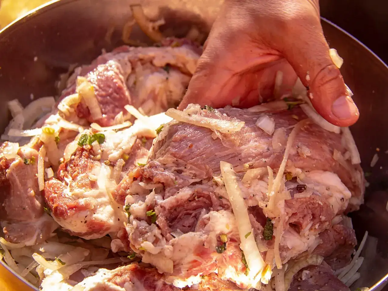 Ręka miesza karkówkę z cebulą i przyprawami. Idealna do pieczenia w odpowiedniej temperaturze.