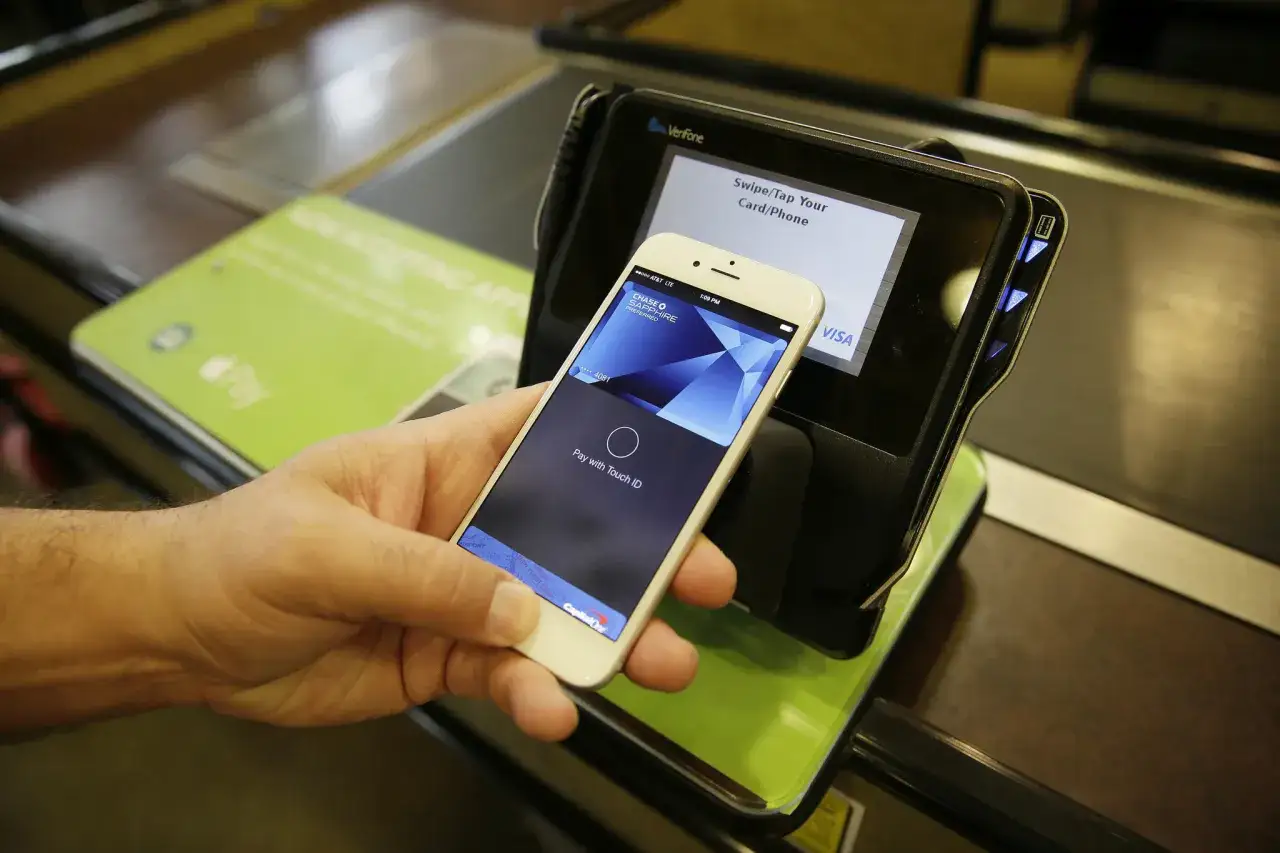 Dłoń trzyma iPhone'a z kartą płatniczą, zbliżając go do terminala. Tak jak płacić Revolutem, szybko i wygodnie.