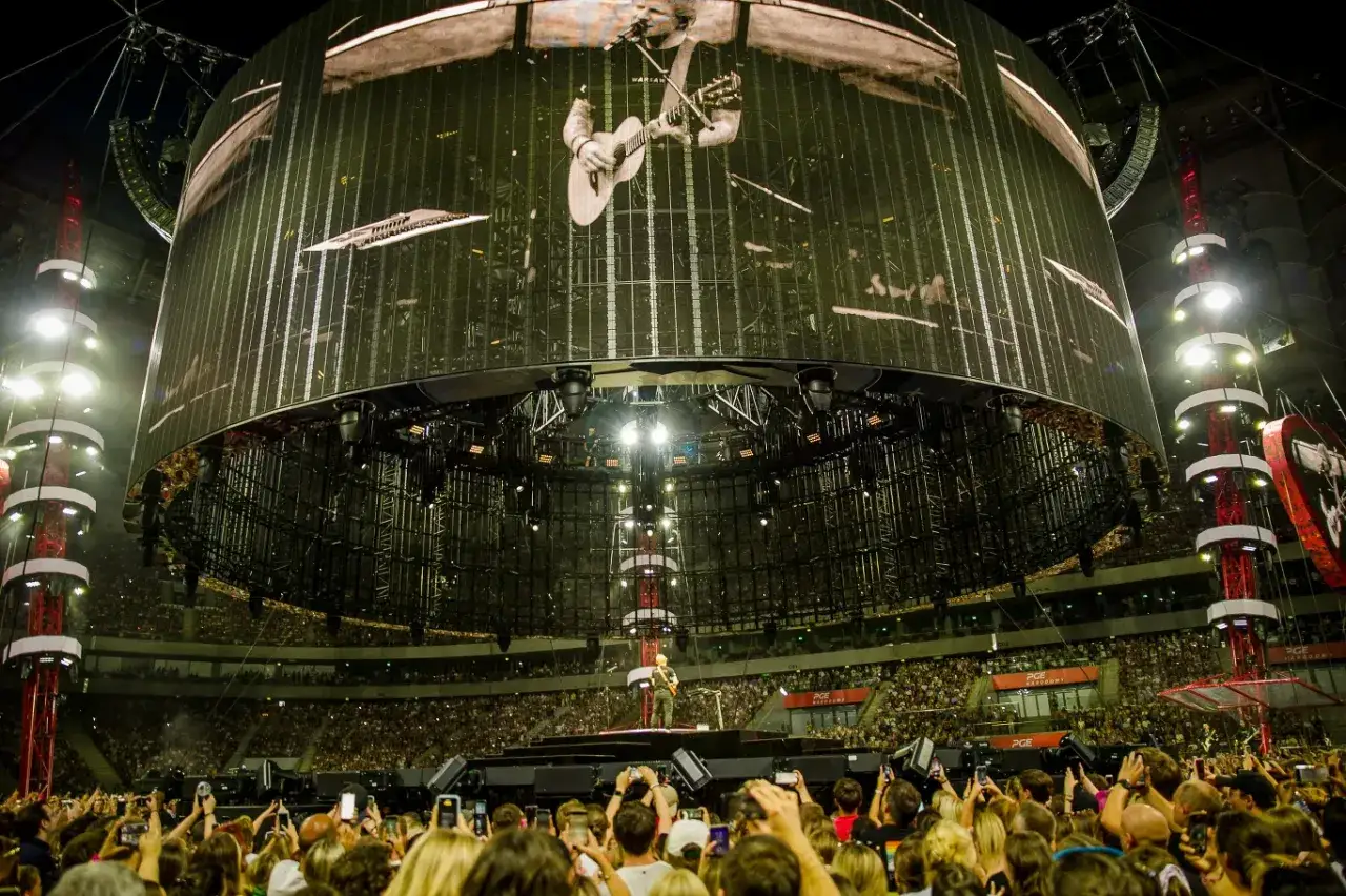 Ed Sheeran w Warszawie zgromadził tłumy. Ogromny ekran pokazuje artystę, a pod nim tysiące fan&oacute;w z telefonami.