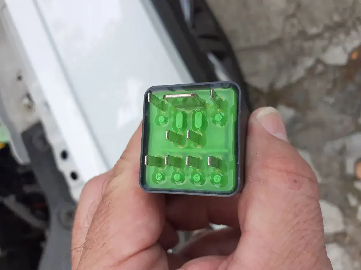 Uszkodzony przekaźnik świec żarowych objawy: zielony element z metalowymi stykami, trzymany w dłoni.
