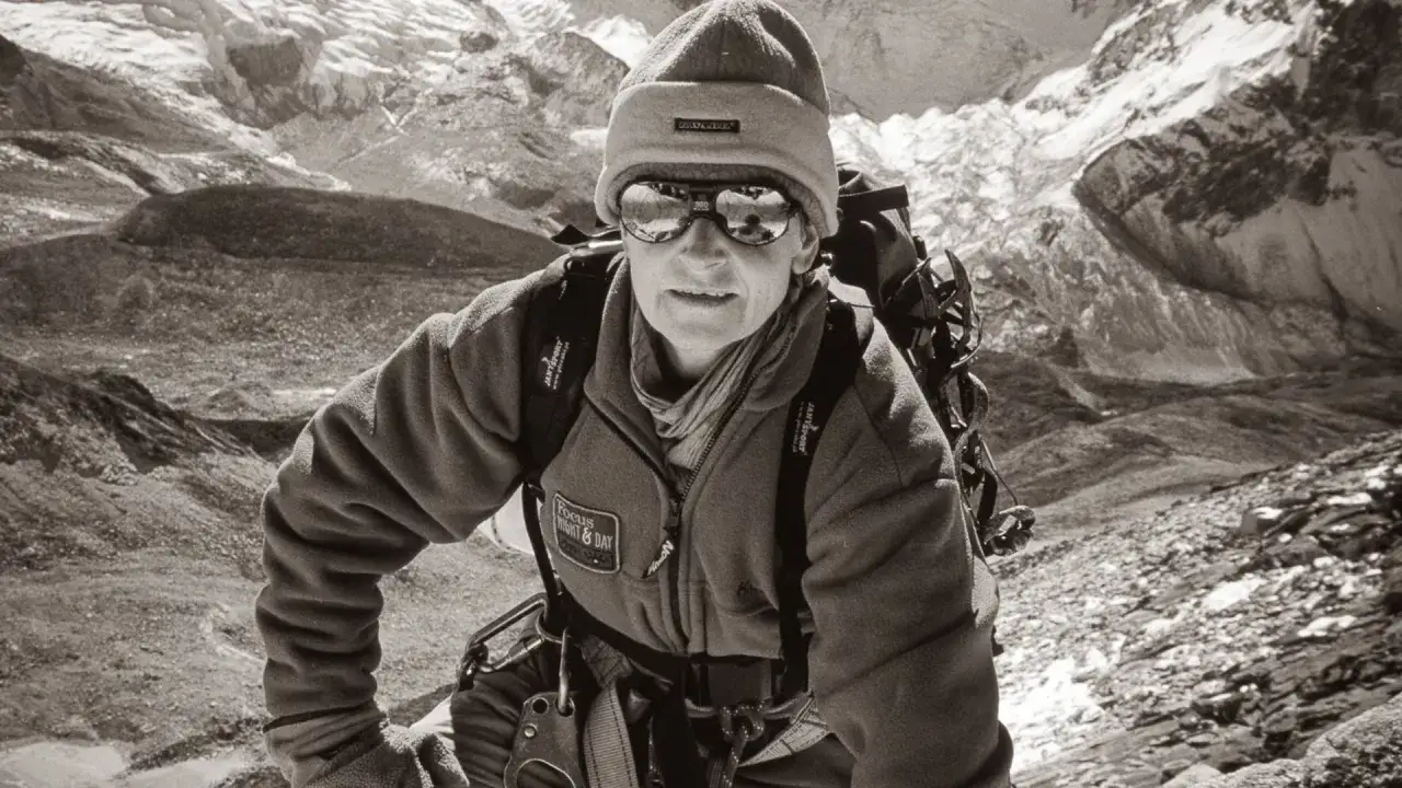 Polska alpinistka w czapce i goglach wspina się po skalistym zboczu. W tle widać ośnieżone szczyty.