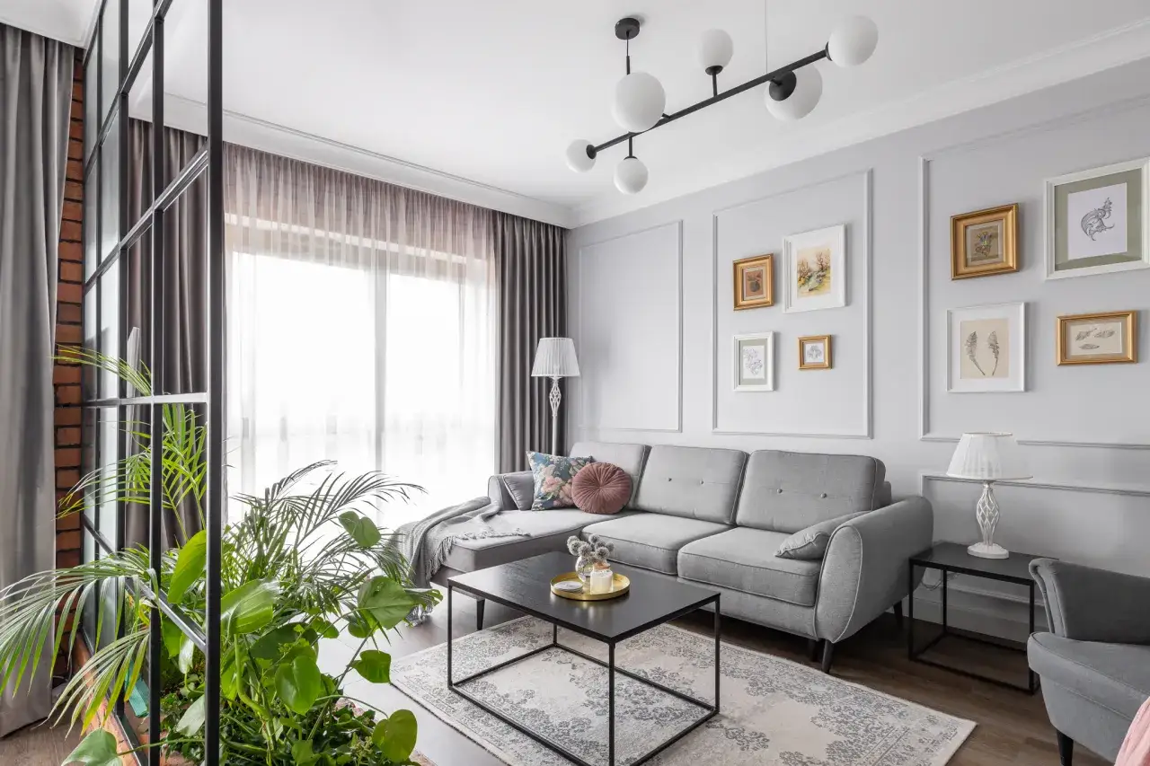 Jasne ściany idealnie komponują się z białymi meblami i szarą kanapą, tworząc przytulną przestrzeń.