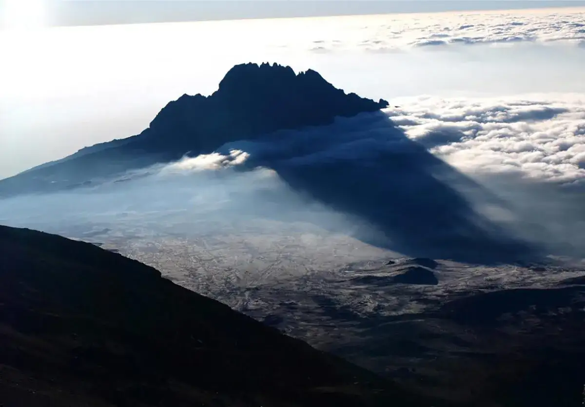Widok z Kilimandżaro. G&oacute;ra rzuca długi cień na morze chmur i pustynny krajobraz poniżej.