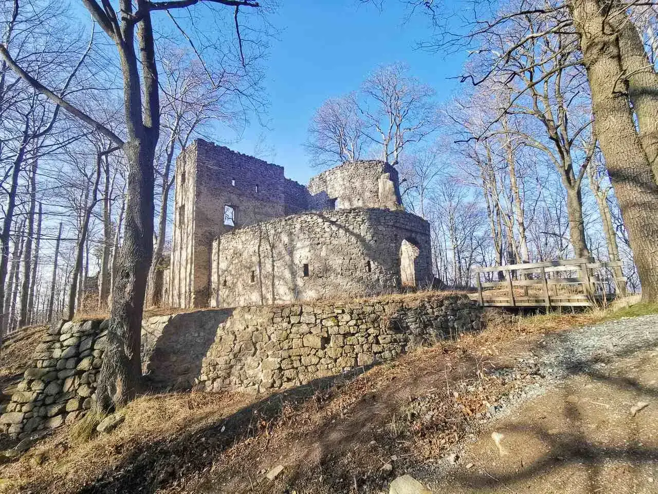 Kamienne ruiny zamku Bolczów w otoczeniu nagich drzew. Drewniany mostek prowadzi do wejścia.