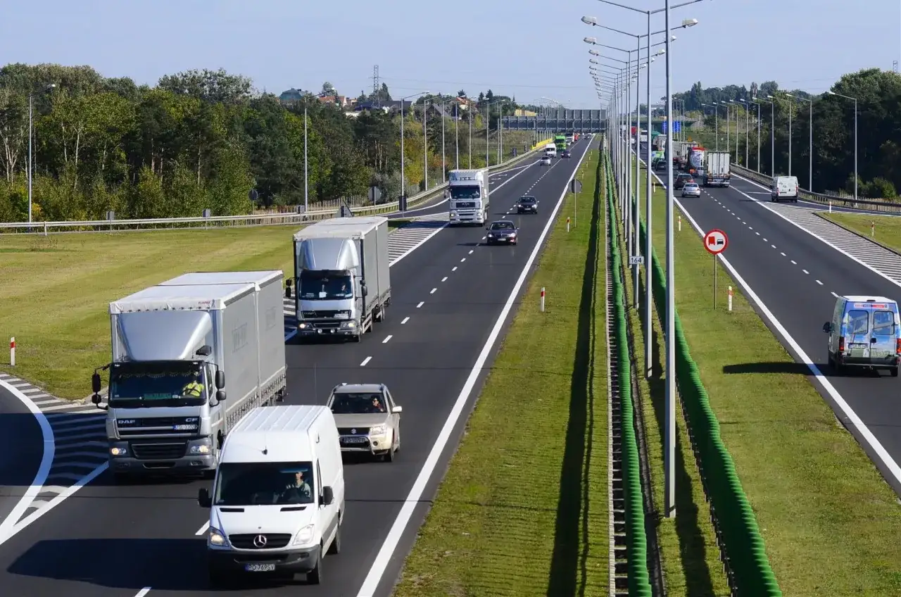 Ruch na drodze jednojezdniowej dwukierunkowej. Ciężarówki i samochody osobowe jadą po pasach ruchu.
