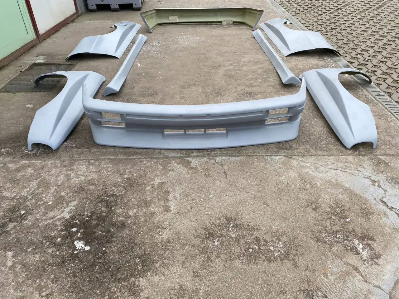 Zestaw części do body kitu BMW E30 M3: zderzak przedni, poszerzenia błotników, progi i spojler tylny.