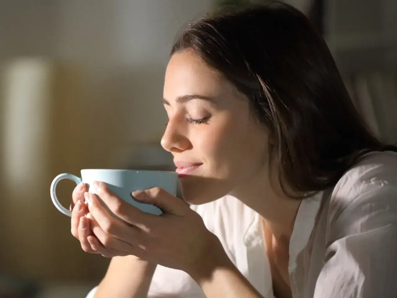 Kobieta zamyka oczy, wdychając aromat kawy. Czy kawa szkodzi na wątrobę? To pytanie nurtuje wielu miłośnik&oacute;w tego napoju.