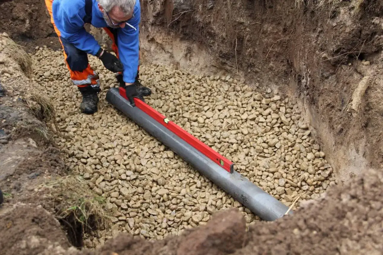Pracownik w okopach sprawdza poziom rury drenarskiej, zasypanej żwirem. Kluczowe dla prawidłowego działania oczyszczalni jest to, jak udrożnić drenaż oczyszczalni.