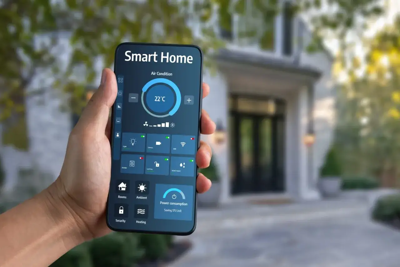 Dłoń trzyma smartfon z aplikacją Smart Home, sterując klimatyzacją i innymi funkcjami domu.