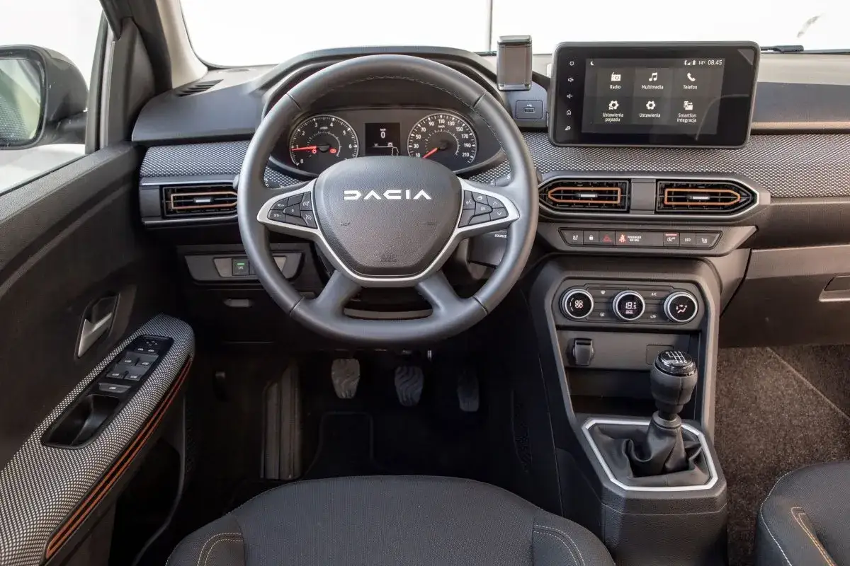 Wnętrze Dacia Sandero Stepway z ekranem multimedialnym, kierownicą i dźwignią zmiany biegów. Dostępne silniki zapewniają ekonomiczną jazdę.
