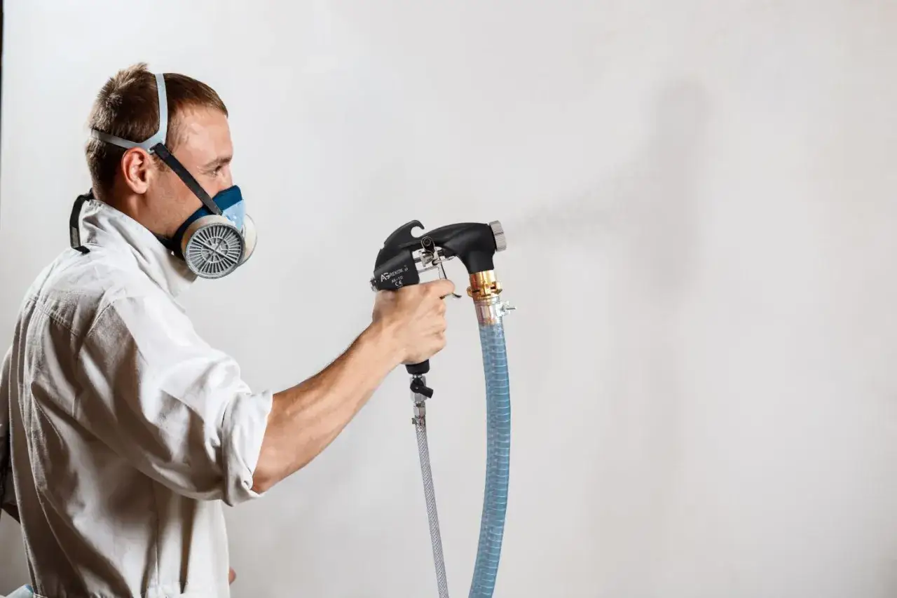 Mężczyzna w masce ochronnej używa agregatu tynkarskiego Graco T Max 506 do natryskiwania tynku na ścianę.