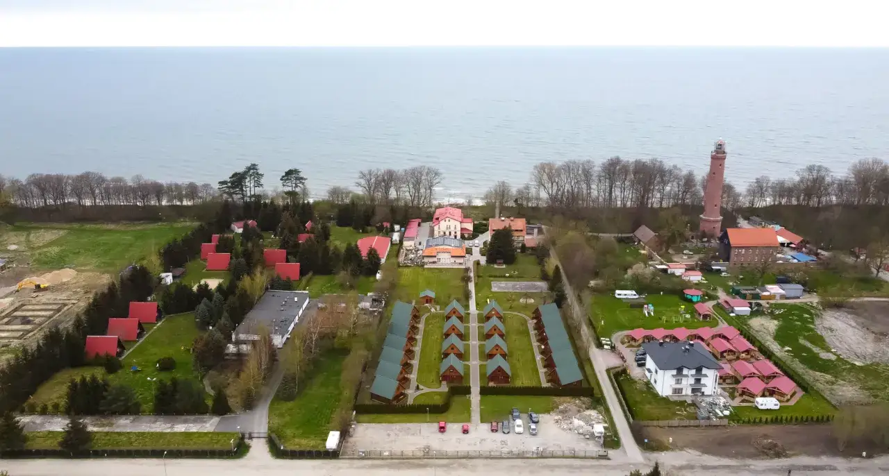 Gąski nad morzem: malowniczy widok na ośrodek wypoczynkowy z domkami, budynkami i latarnią morską w tle.