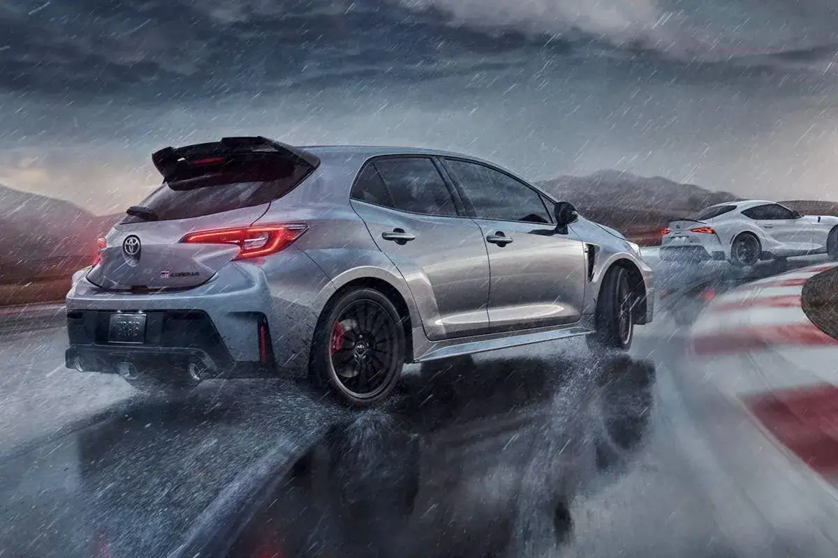 Srebrna Toyota Corolla GR na torze wyścigowym podczas deszczu. Obok niej biała Toyota Supra.