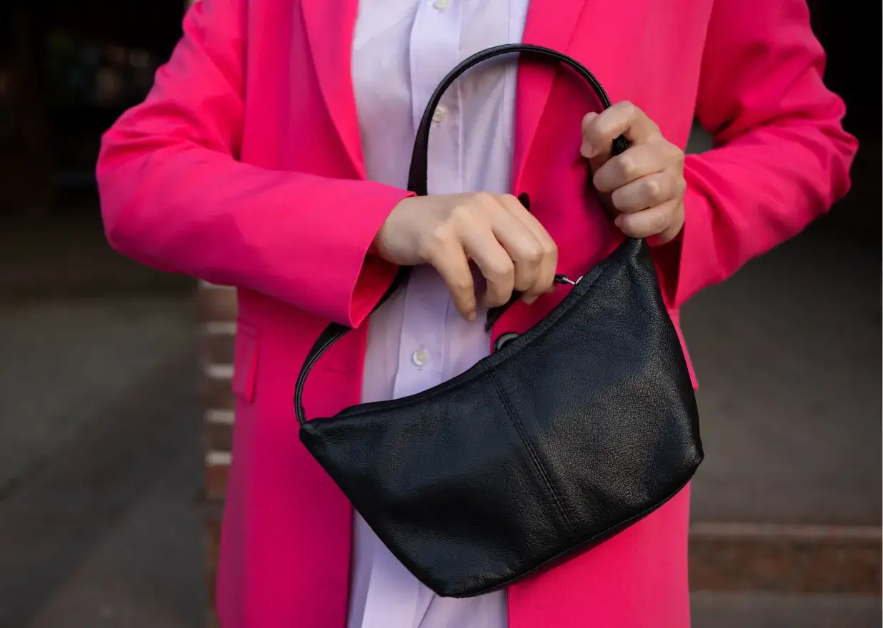 Kobieta w różowej marynarce trzyma czarną, skórzaną torebkę. Idealna na lato, ta modna torebka dodaje stylu każdej stylizacji.