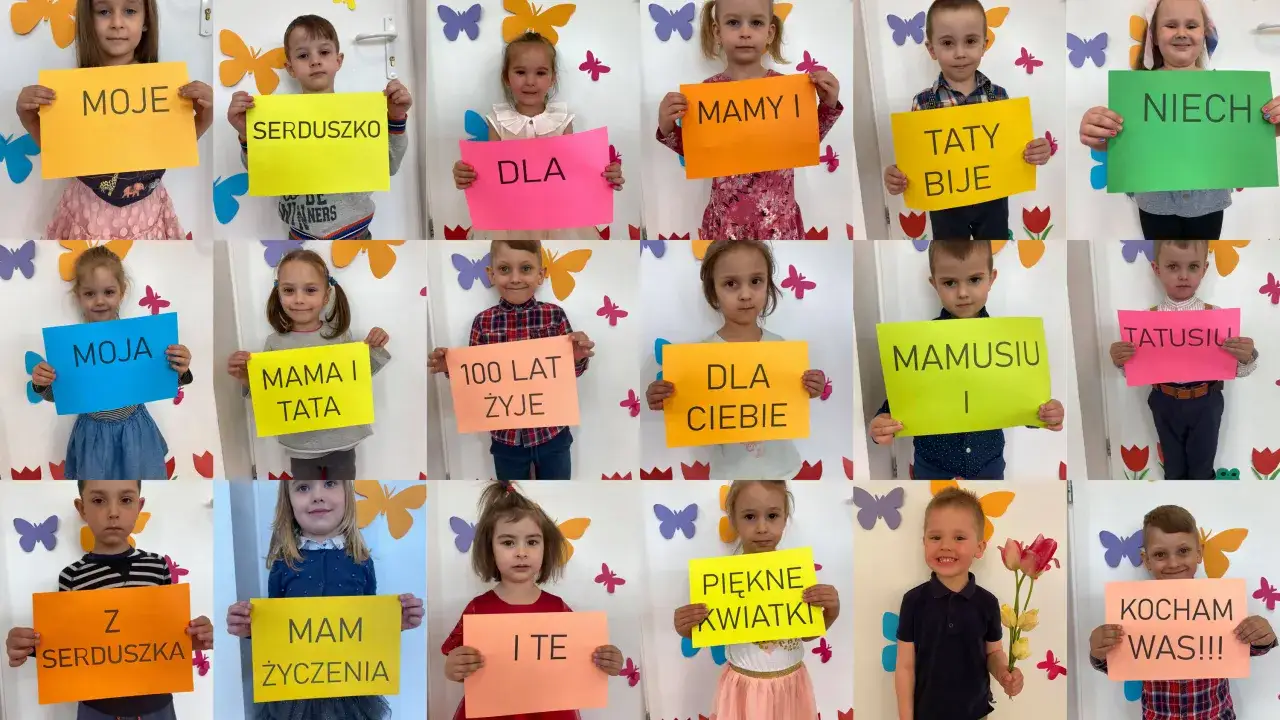Dzieci w przedszkolu świętują dzień mamy, trzymając kolorowe kartki z napisami: 