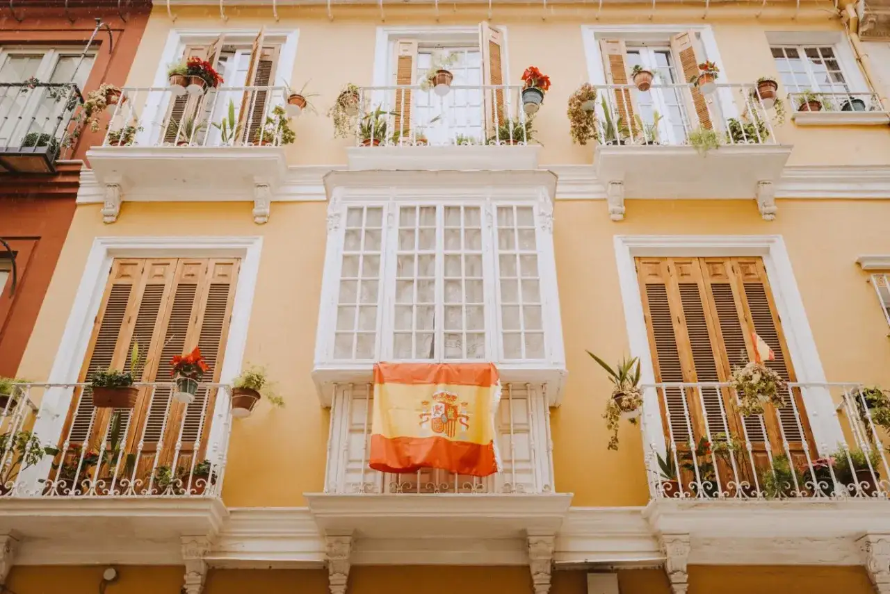 Żółta kamienica z balkonami i hiszpańską flagą. Czy Airbnb jest bezpieczne? Tak, jeśli wybierasz sprawdzone oferty.