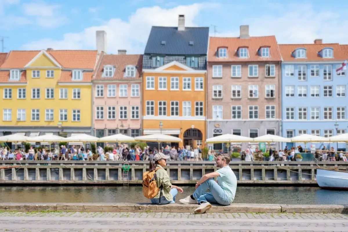 Para co zwiedzić w Kopenhadze, para siedzi nad kanałem, podziwiając kolorowe kamienice i gwarne kawiarnie.