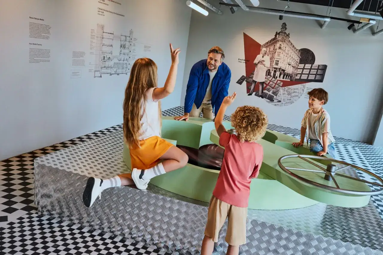 Rodzina bawi się przy interaktywnej wystawie w Muzeum Czekolady Warszawa. Dzieci z ciekawością obserwują wirującą czekoladę.