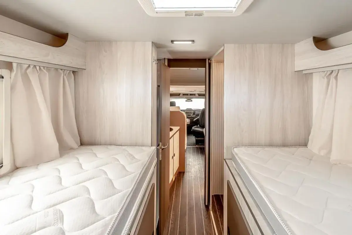 Wnętrze kampera z dwoma ł&oacute;żkami, widok na kabinę kierowcy. Idealny kamper tanio na wakacyjne wyprawy.