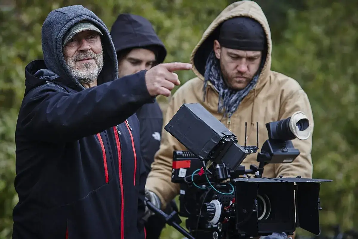 Reżyser filmu Jancio Wodnik, z brodą i w kapturze, wskazuje palcem na ekipę filmową pracującą przy kamerze.