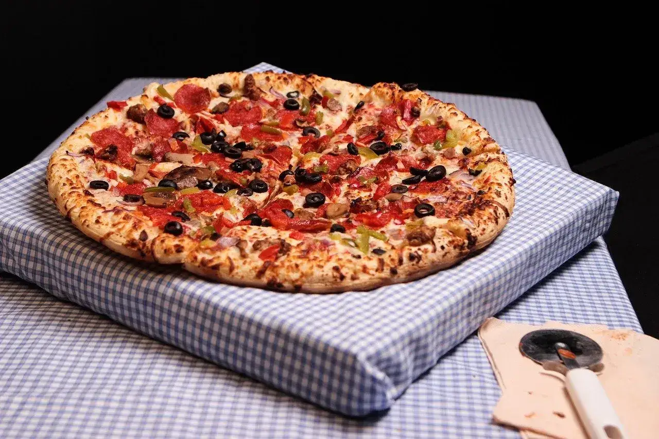 Pyszna pizza z pepperoni, oliwkami i warzywami, gotowa do krojenia po leżakowaniu ciasta.