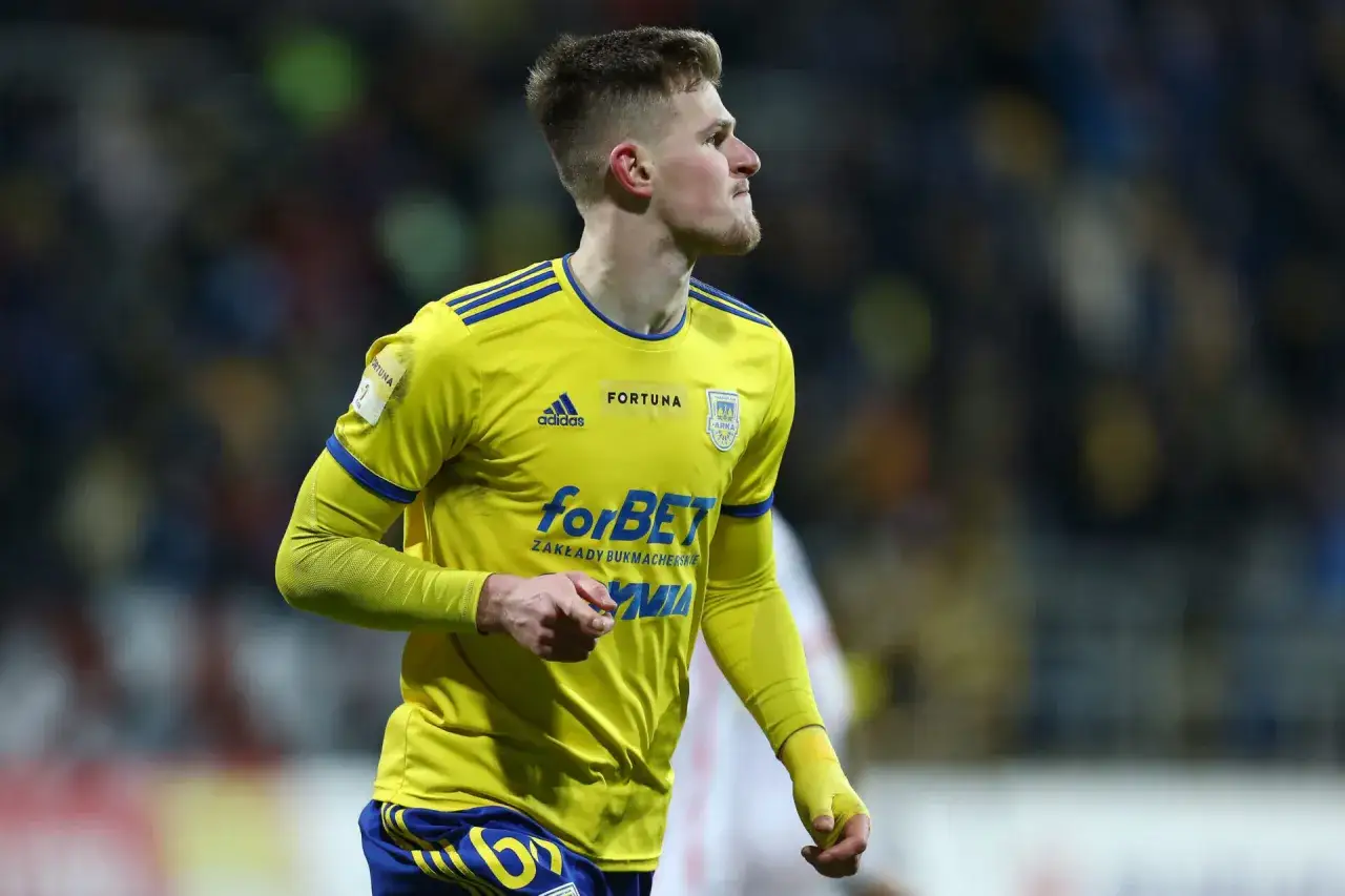 Piłkarz w żółtej koszulce z niebieskimi pasami, z logo Arki Gdynia, walczy o awans. Ile drużyn wchodzi do ekstraklasy?