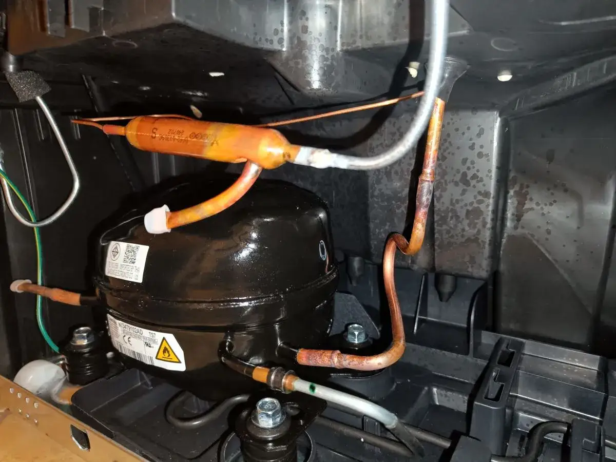 Kompresor lod&oacute;wki głośno chodzi, widać miedziane rurki i filtr.