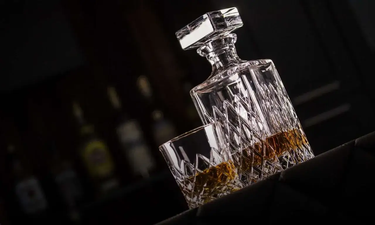 Kryształowa karafka i szklanka z whisky. Czy whisky podnosi ciśnienie? W tle butelki alkoholi.